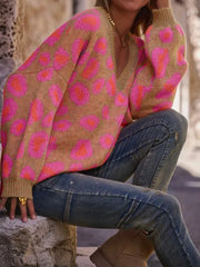 Woman wearing Leopard Oversized V-Neck Sweater with pink leopard print and casual jeans, sitting stylishly outdoors.