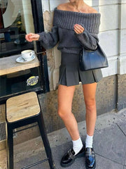 Woman wearing Off-Shoulder Ribbed Long Sleeve Sweater in urban setting, paired with mini skirt and loafers, holding a black handbag.