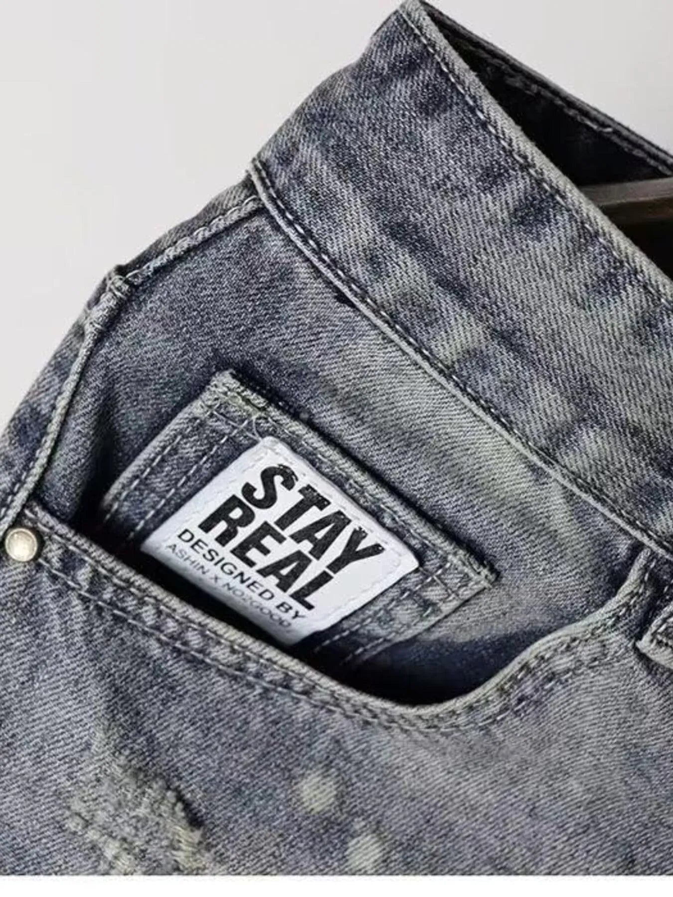 Close-up of pocket on men's denim shorts featuring 'STAY REAL' label and distressed texture.