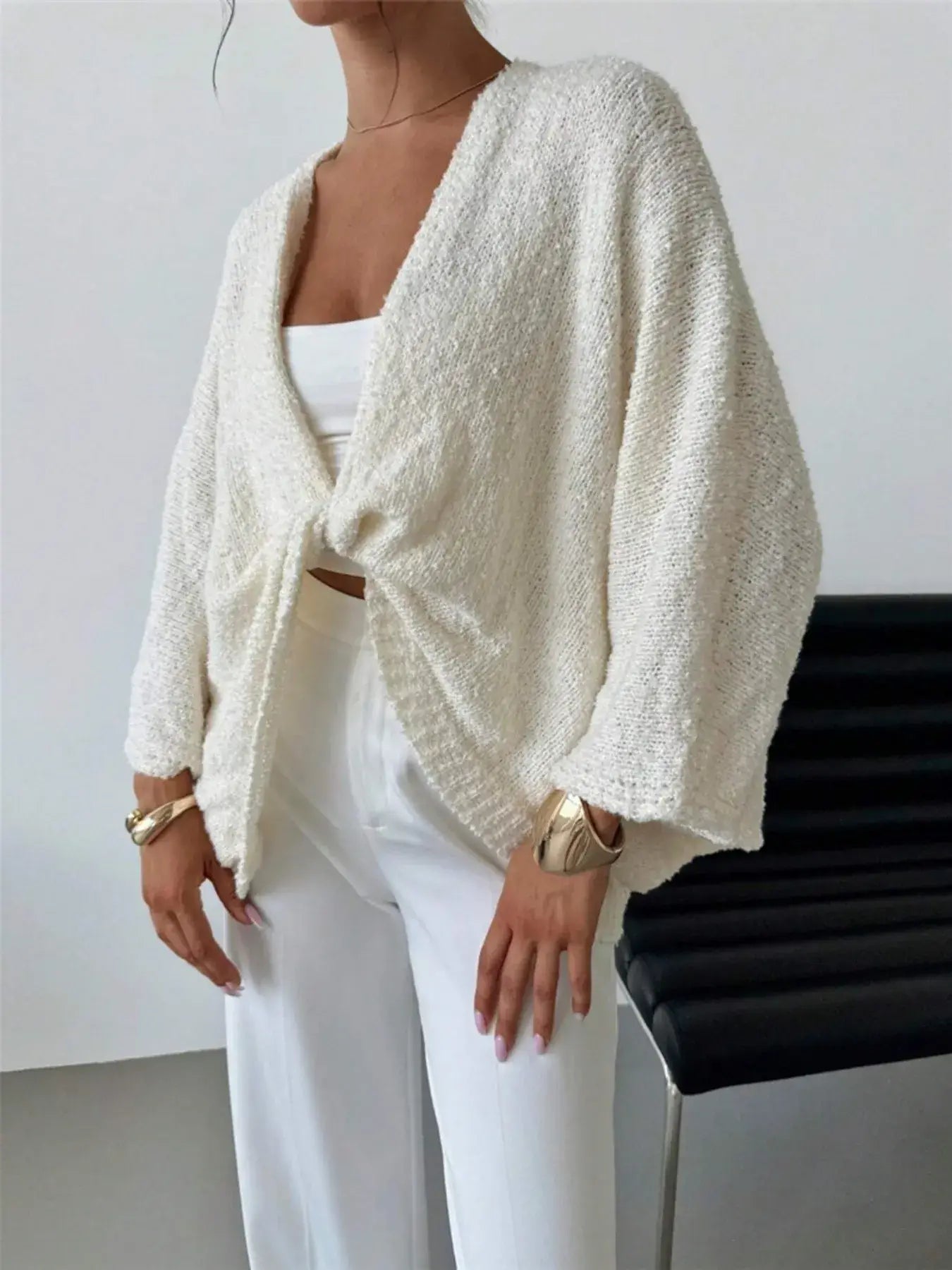 Woman wearing a twist-front textured knit cardigan in ivory, featuring a relaxed fit, paired with white pants and accessories.