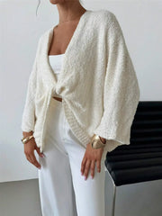 Woman wearing a twist-front textured knit cardigan in ivory, featuring a relaxed fit, paired with white pants and accessories.