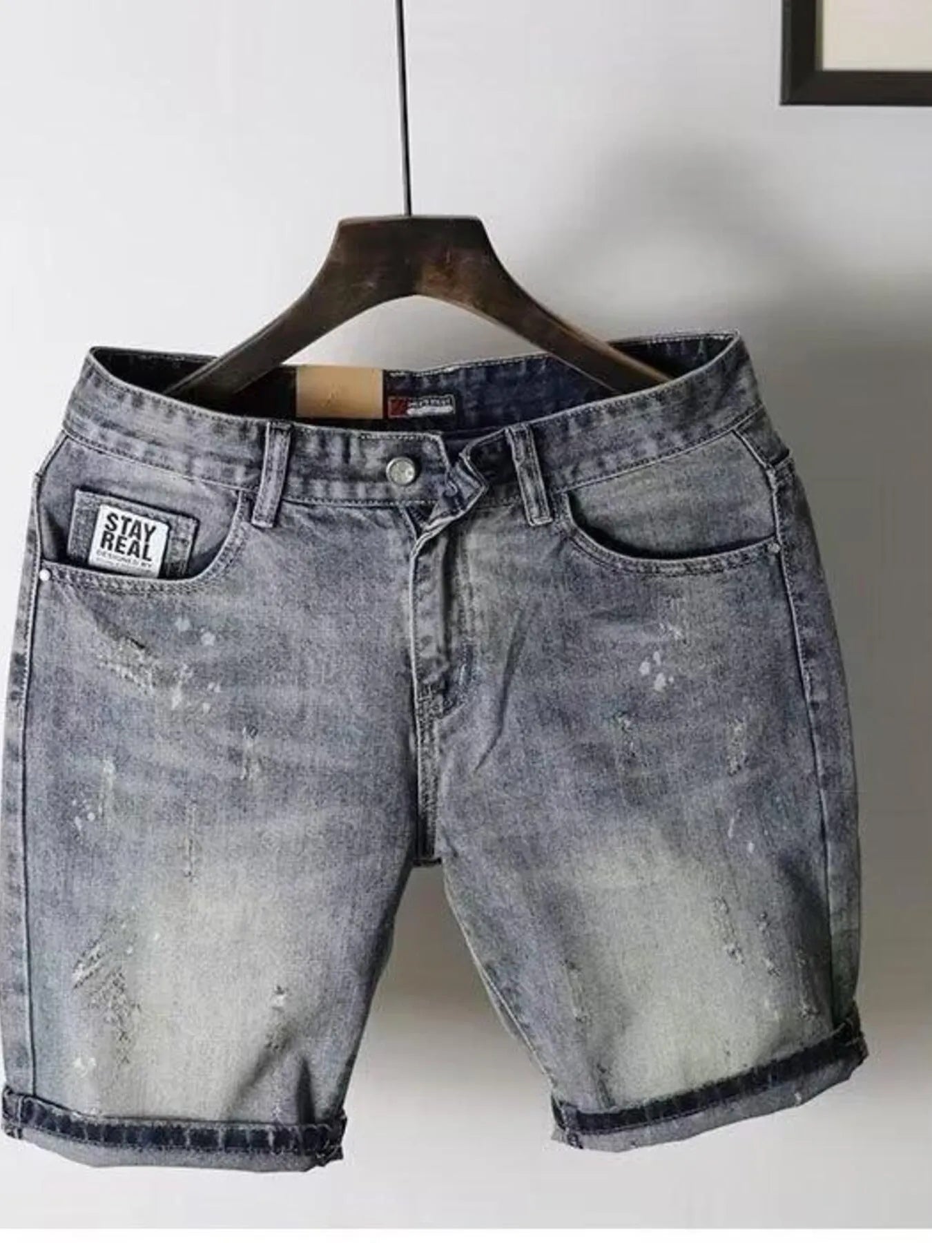 Men's pocketed denim shorts on a hanger, featuring a faded wash and slight distressing, ideal for casual wear.