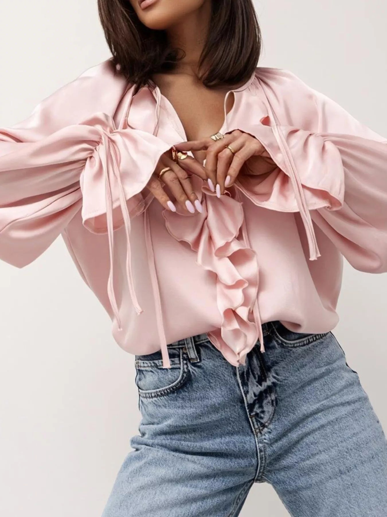 Woman wearing Ruffle Trim Satin Flounce Sleeve Blouse in pink with denim jeans, featuring soft tie-neck and cascading ruffles.