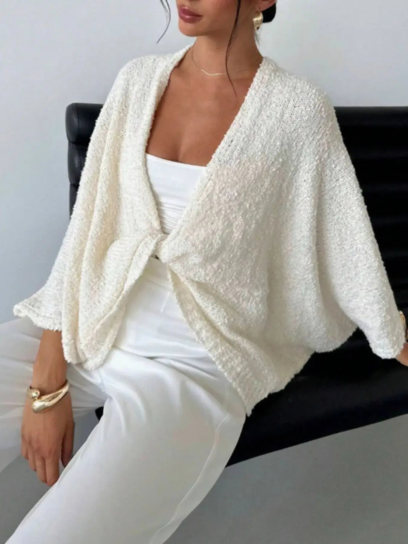 Woman wearing a modern chic twist-front textured knit cardigan in ivory, displaying a stylish and relaxed fit for elegant layering.