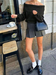 Woman wearing Off-Shoulder Ribbed Long Sleeve Sweater with black handbag and pleated skirt, standing at a café.