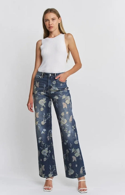 Woman wearing Floral High-Rise Wide-Leg Jeans with floral print, paired with a white sleeveless top, standing against a white background.