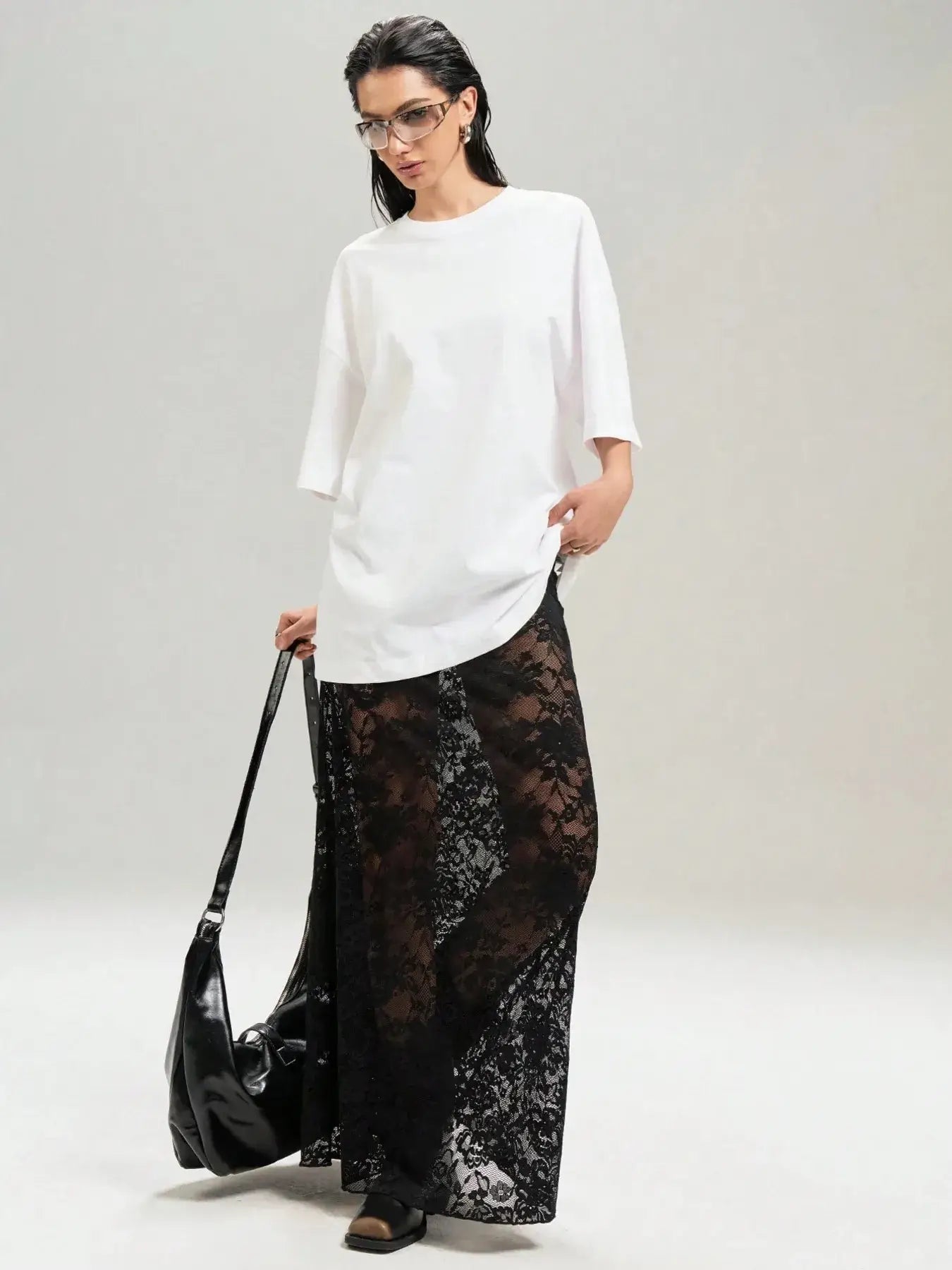 Model wearing chic lace maxi skirt with sheer design in black, paired with white top and carrying black bag, showcasing versatile fashion.
