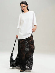 Model wearing chic lace maxi skirt with sheer design in black, paired with white top and carrying black bag, showcasing versatile fashion.