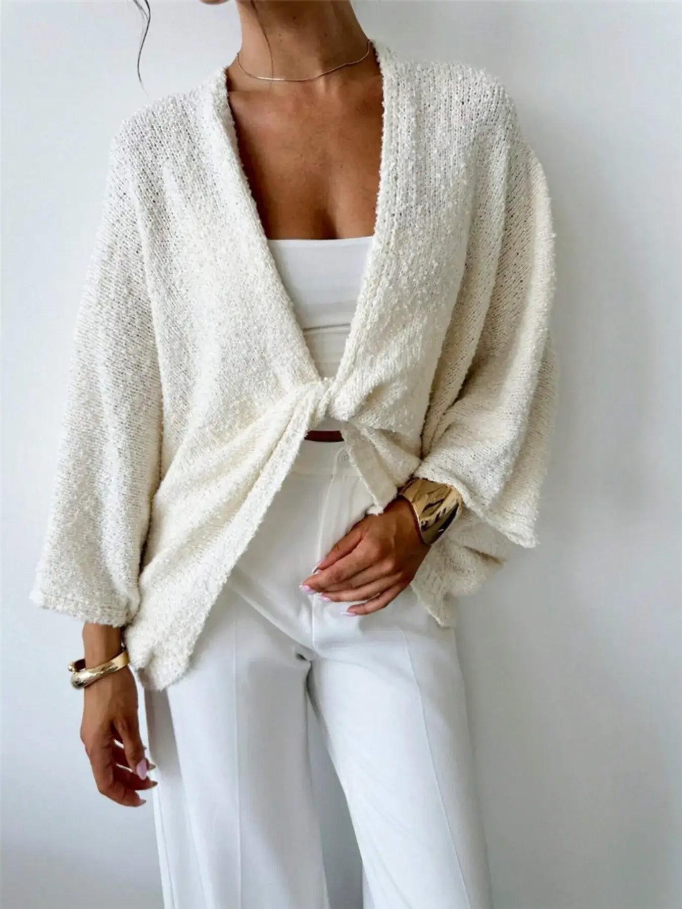 Model wearing a cream twist-front textured knit cardigan paired with white pants, showcasing a chic and modern style.