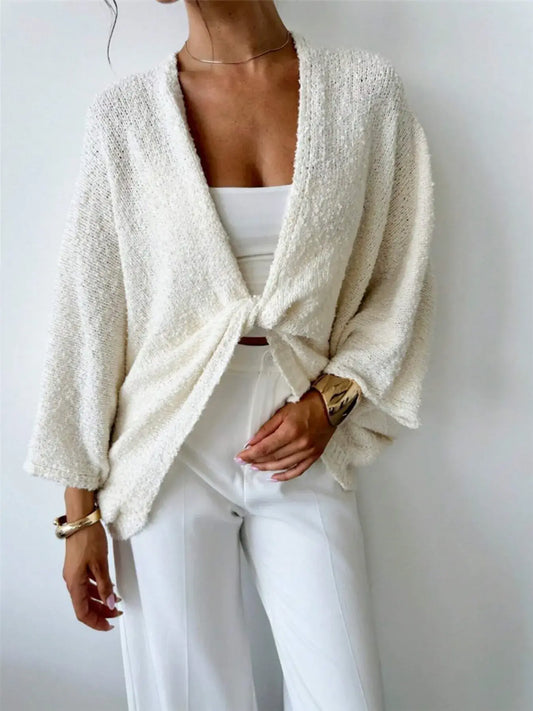 Model wearing a cream twist-front textured knit cardigan paired with white pants, showcasing a chic and modern style.