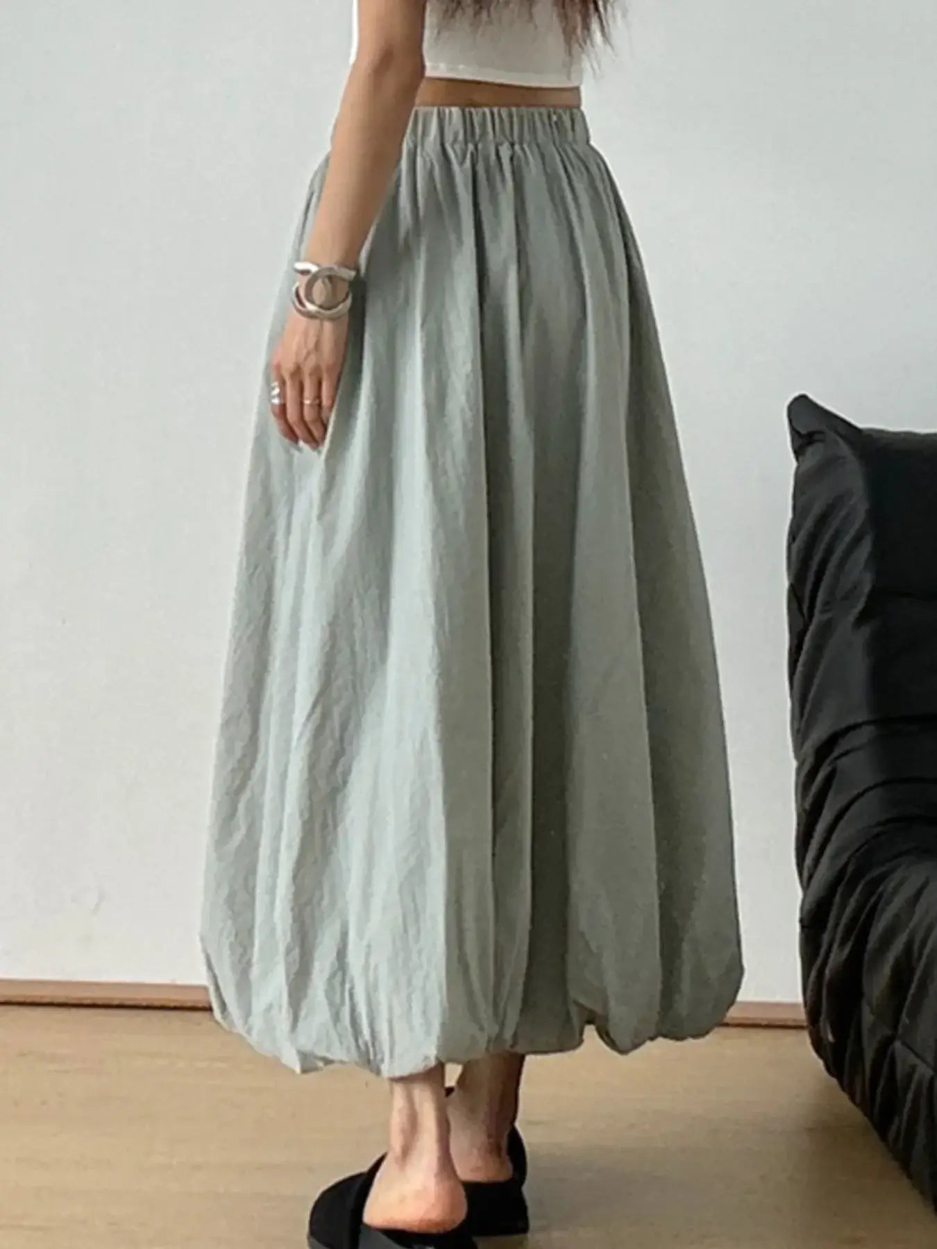 Woman wearing an elastic waist bubble hem maxi skirt in a minimalist room, showcasing its paperbag waist and effortless style.