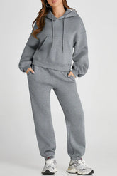 Woman wearing gray Dropped Shoulder Hooded Top and Pants Active Set with drawstring and pockets, made from polyester and cotton mix.