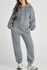 Woman wearing gray Dropped Shoulder Hooded Top and Pants Active Set with drawstring and pockets, made from polyester and cotton mix.