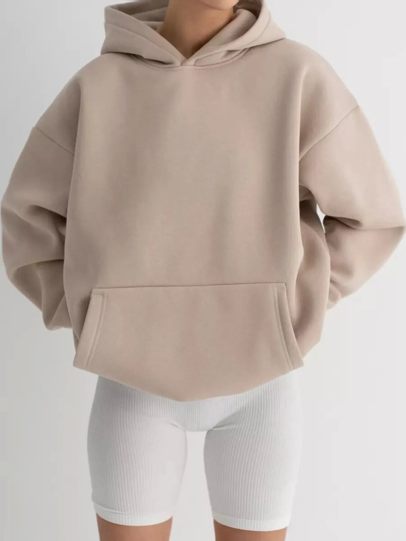 Kangaroo Pocket Long Sleeve Hoodie in beige with convenient pockets, slightly stretchy polyester-spandex blend, modeled with white shorts.