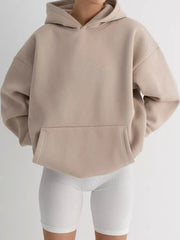 Kangaroo Pocket Long Sleeve Hoodie in beige with convenient pockets, slightly stretchy polyester-spandex blend, modeled with white shorts.