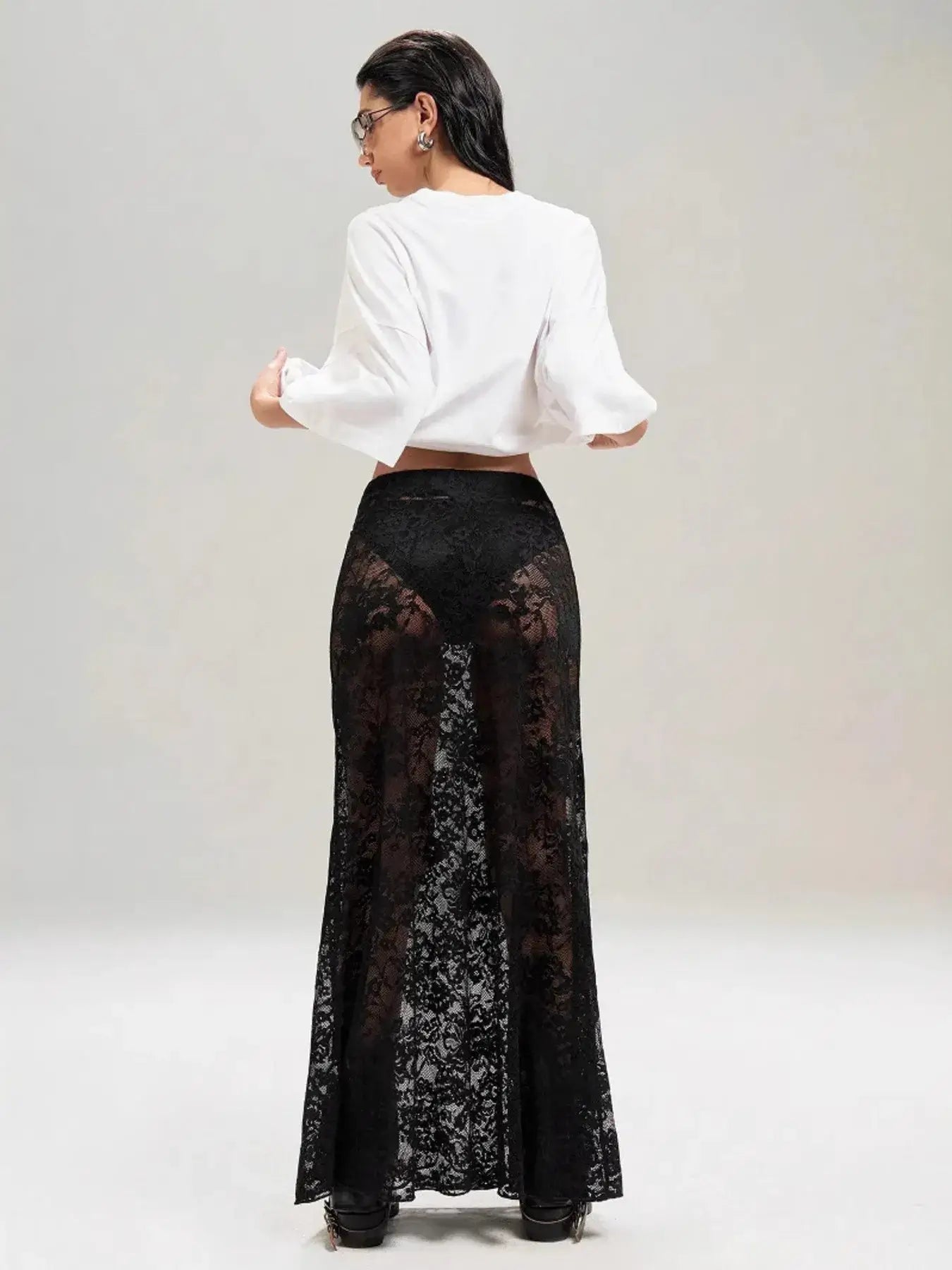 Model wearing stylish sheer black lace maxi skirt with elegant design, perfect for layering over bodysuits or swimwear.