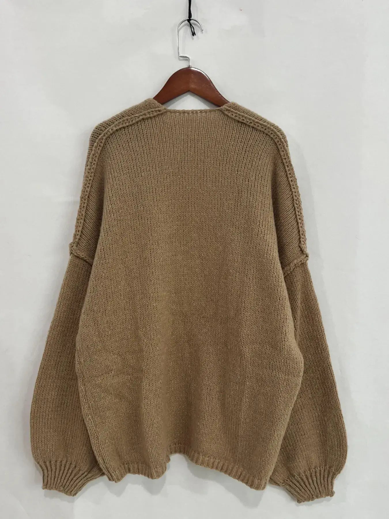 Back view of an oversized textured beige open front dropped shoulder cardigan with voluminous sleeves, hung on a wooden hanger.