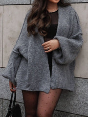 Woman wearing a grey oversized open front dropped shoulder cardigan with voluminous sleeves, paired with a chic outfit, holding a bag.