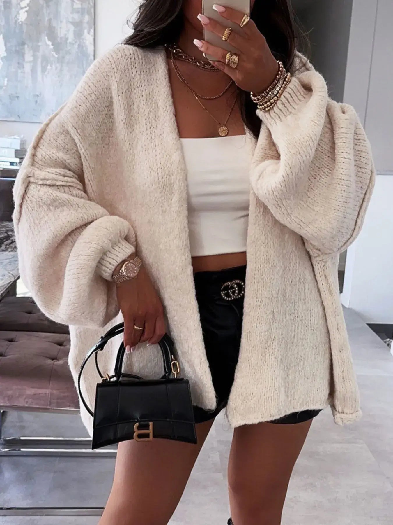 Model wearing oversized open front dropped shoulder cardigan with voluminous sleeves, styled with a white crop top and black mini bag.