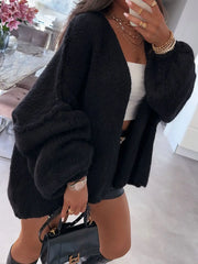 Woman wearing black open front dropped shoulder cardigan with oversized sleeves, accessorized with jewelry and holding a handbag.