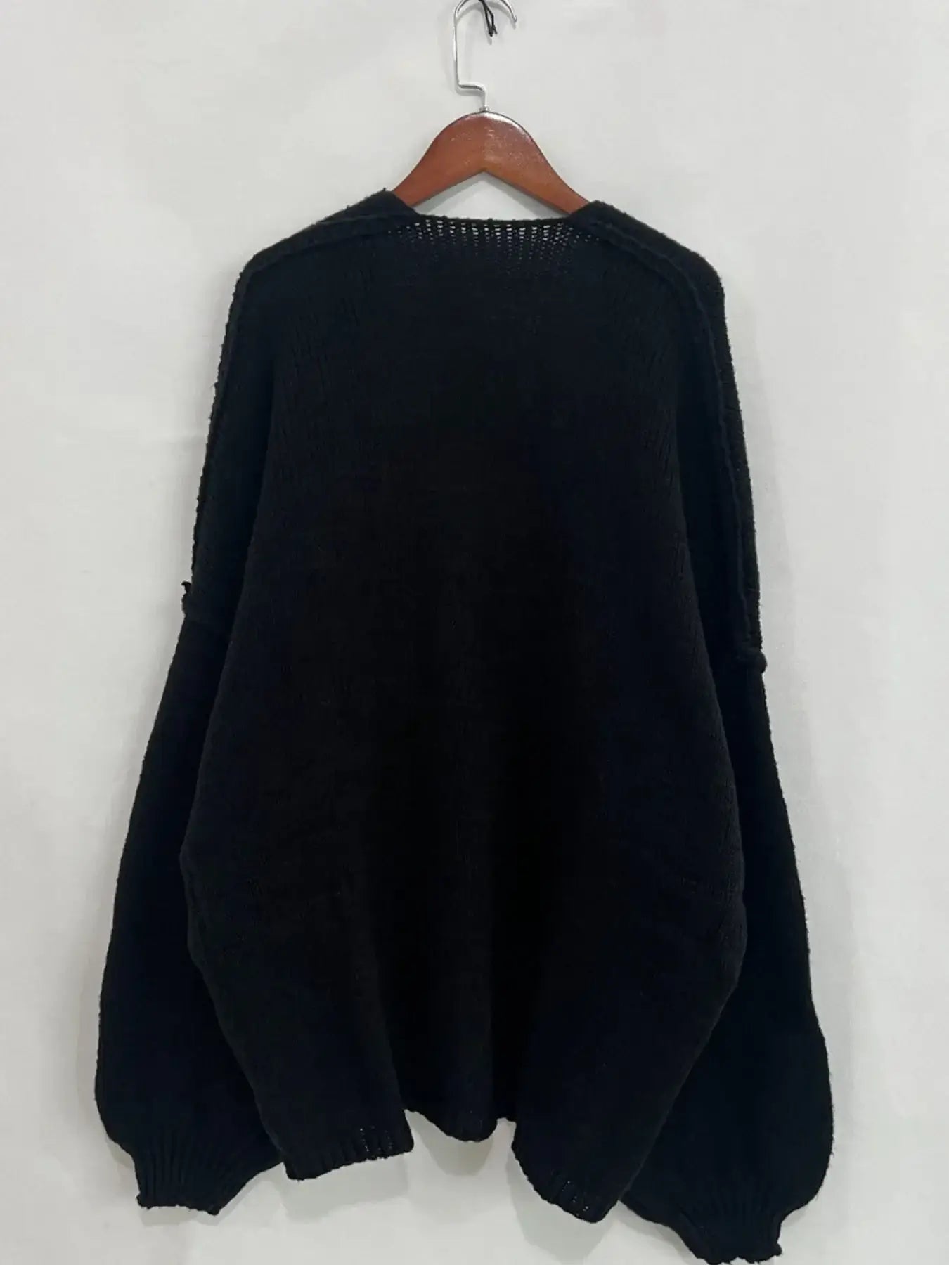 Back view of an oversized black open front dropped shoulder cardigan hanging on a wooden hanger, showcasing its textured fabric.