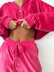 Model wearing pink velour zip-up hoodie and jogger set with drawstring waist, showcasing a stylish and comfortable lounge outfit.