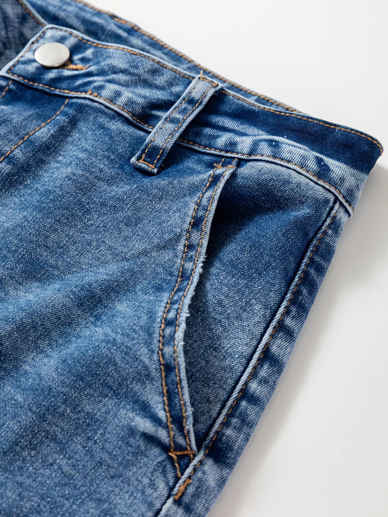 Detail view of blue denim loose fit cropped jeans with seam detailing and button closure.