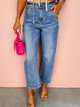 Woman wearing denim seam detail loose fit cropped jeans with a pink bag and sandals against a peach background.