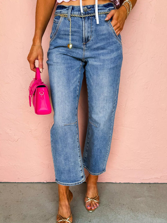 Woman wearing denim seam detail loose fit cropped jeans with a pink bag and sandals against a peach background.