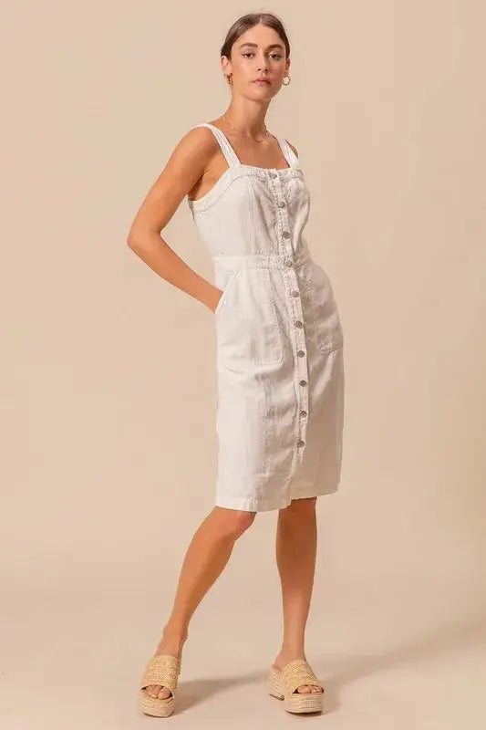 Lightweight cotton pinafore dress with button front and pockets, styled for a relaxed and timeless look.