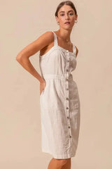 Pinafore dress with front buttons and pockets, styled for comfort and versatility in a neutral cotton fabric.
