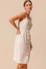 Side profile of button down pinafore dress with cinched waist and front pockets, made from breathable cotton.