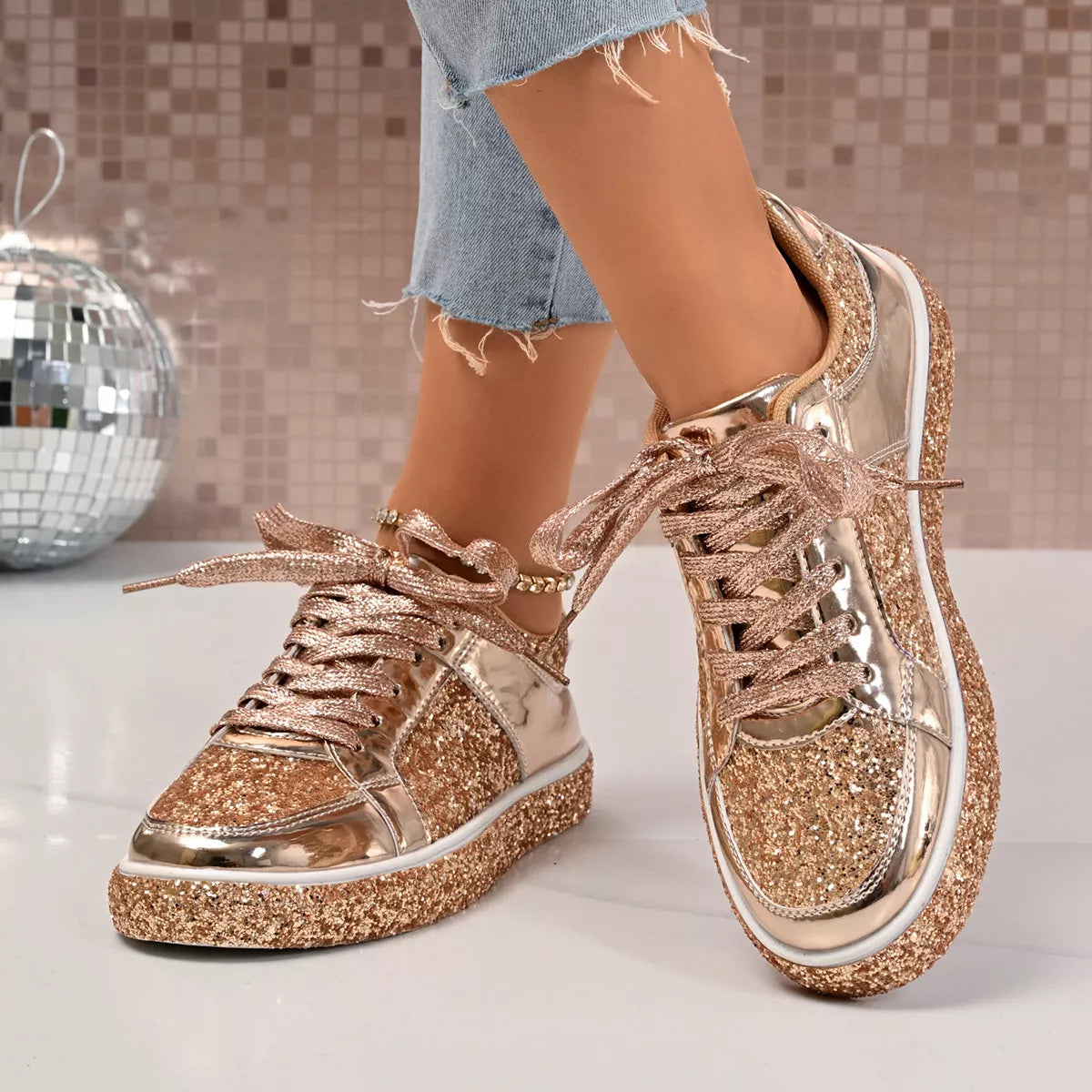 Gold sequin lace up sneakers with PU leather and rubber sole, highlighting fashionable flat design, worn with jeans on white background.