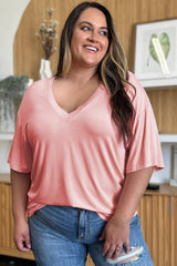 Smiling plus-size model in blush pink Basic Bae Full Size Bamboo V-Neck Drop Shoulder T-Shirt, showcasing its flattering V-neck and soft fabric.