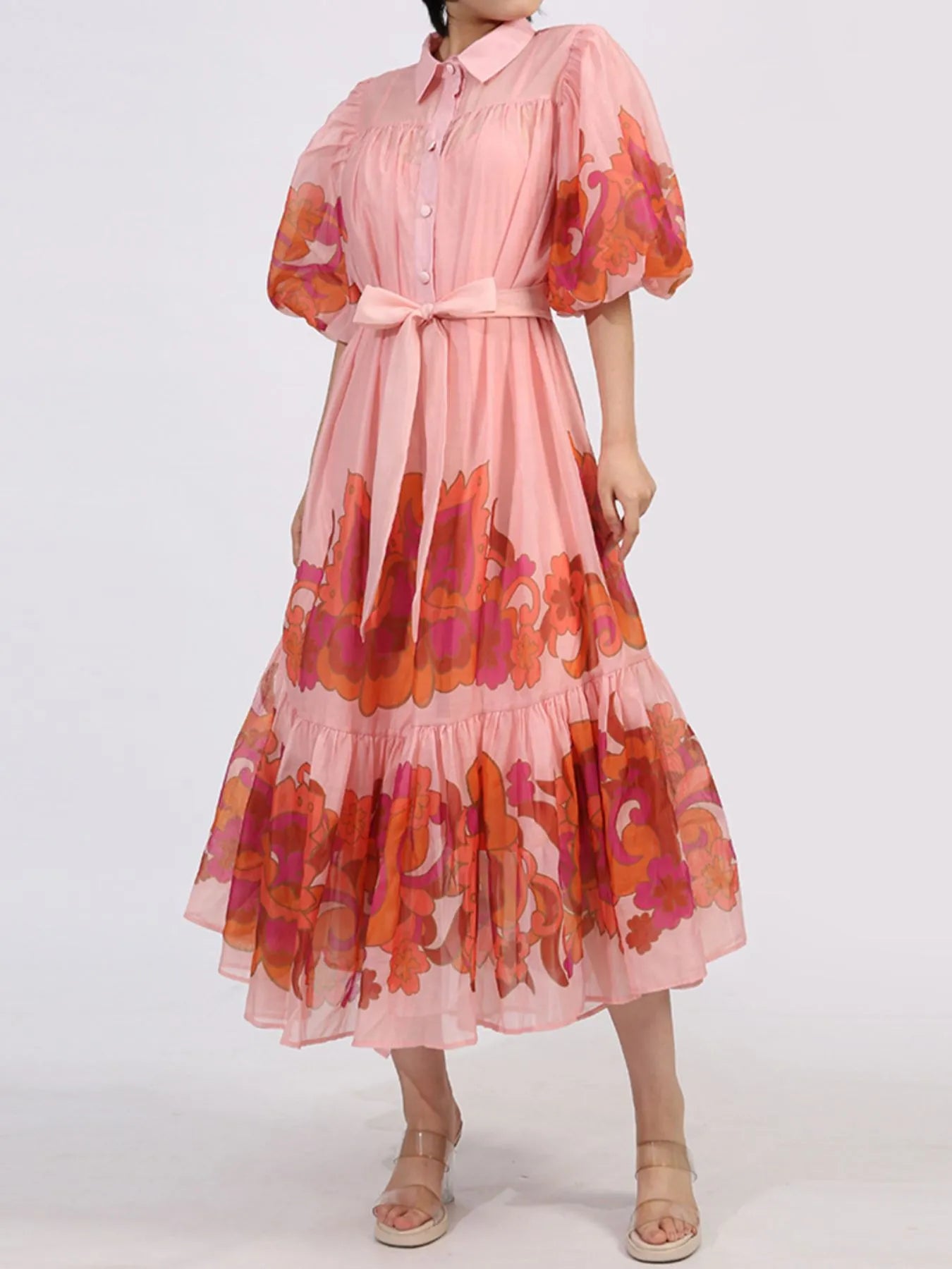 Blush button front puff sleeve dress with bold floral accents, belted waist, and tiered ruffle hem. Perfect for romantic evenings.