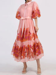 Blush button front puff sleeve dress with bold floral accents, belted waist, and tiered ruffle hem. Perfect for romantic evenings.