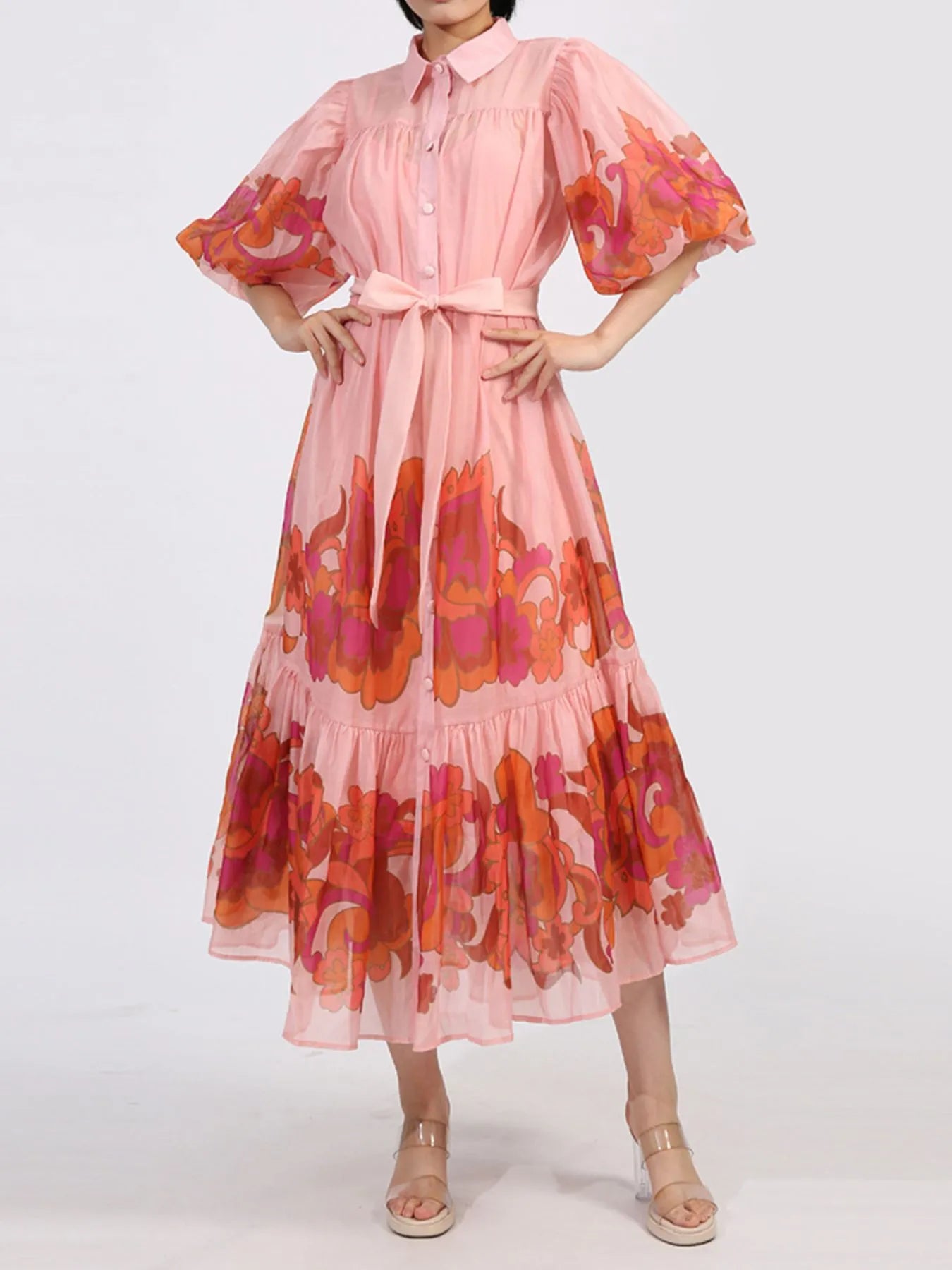 Floaty pink button front dress with puff sleeves and floral accents, featuring a belted waist and tiered ruffle hem. Perfect for elegant occasions.