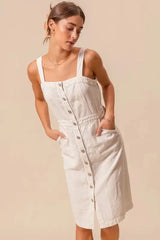 Front angled view of button down pinafore dress with large patch pockets and structured cotton design.