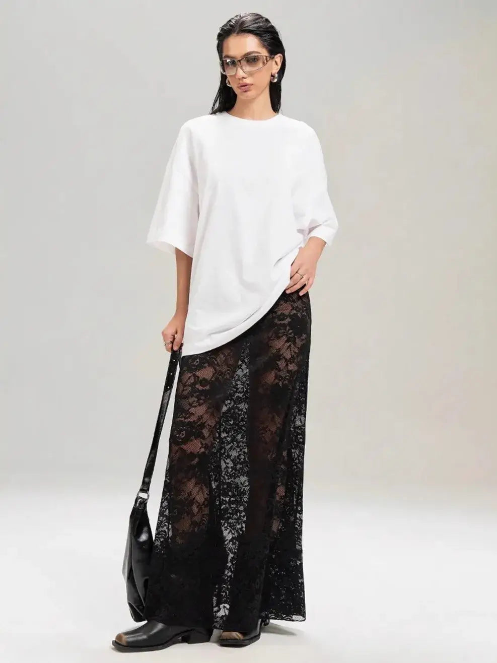 Model wearing a stylish lace maxi skirt with a white top, showcasing a chic and edgy fashion look.