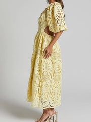 Woman wearing a yellow cutout back lace crochet V-neck dress with intricate detailing and puff sleeves, side view.