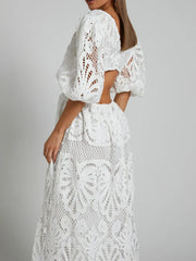 Woman wearing a white lace crochet dress with a cutout back and V-neck, showcasing intricate design details and sophistication.