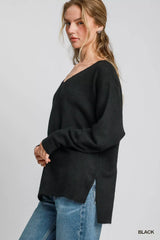 Woman wearing Umgee Wool Blended Pullover Sweater with oversized V-neck in black, paired with blue jeans, side view