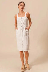 Front-facing view of button down pinafore dress with pockets, styled with neutral sandals for a minimalist look.