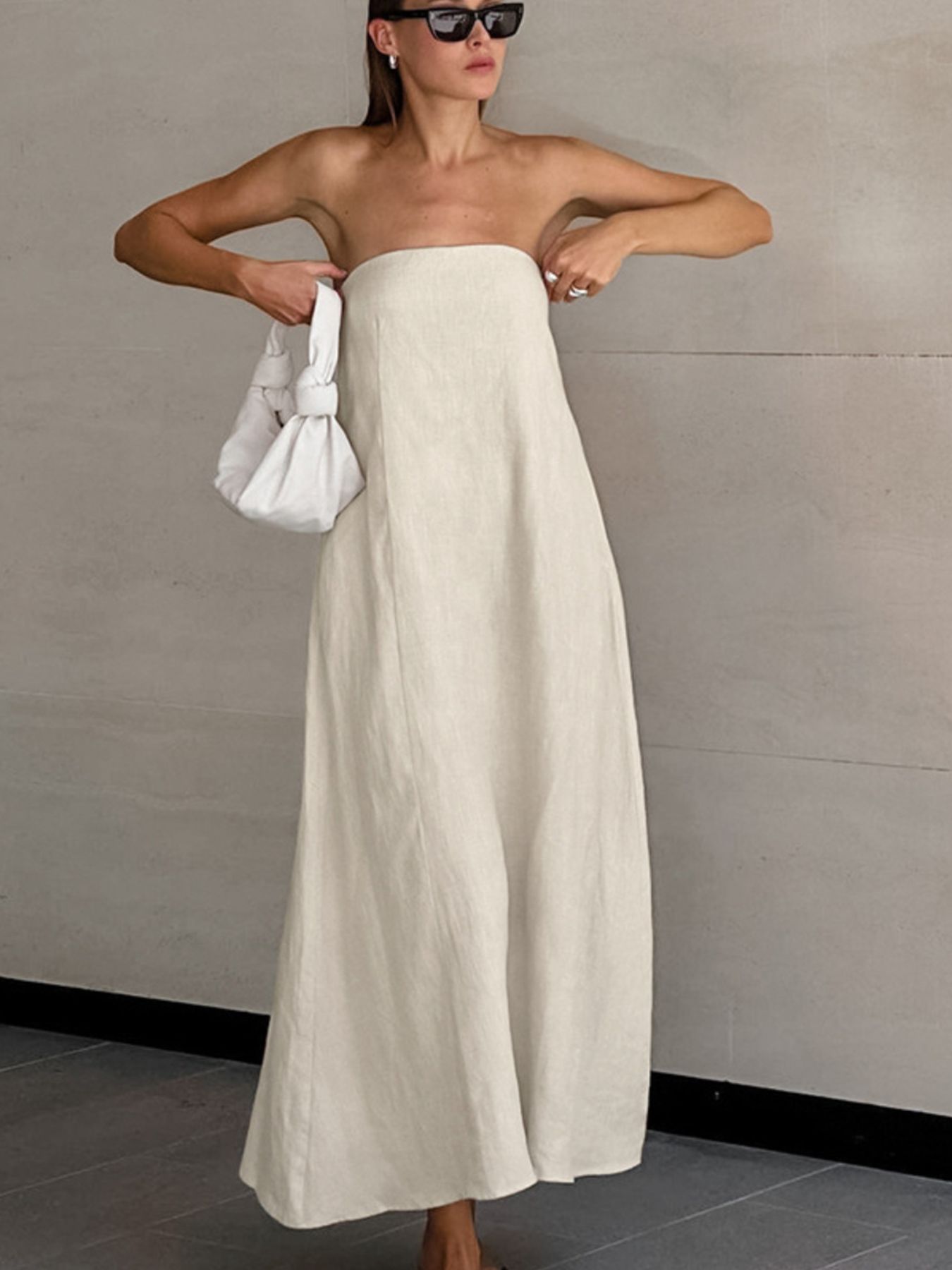 Model wearing a Smocked Back Tube Dress in cream color, paired with a white bag and sunglasses.