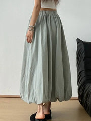 Woman wearing an elastic waist bubble hem maxi skirt in a minimalist room, showcasing its paperbag waist and effortless style.