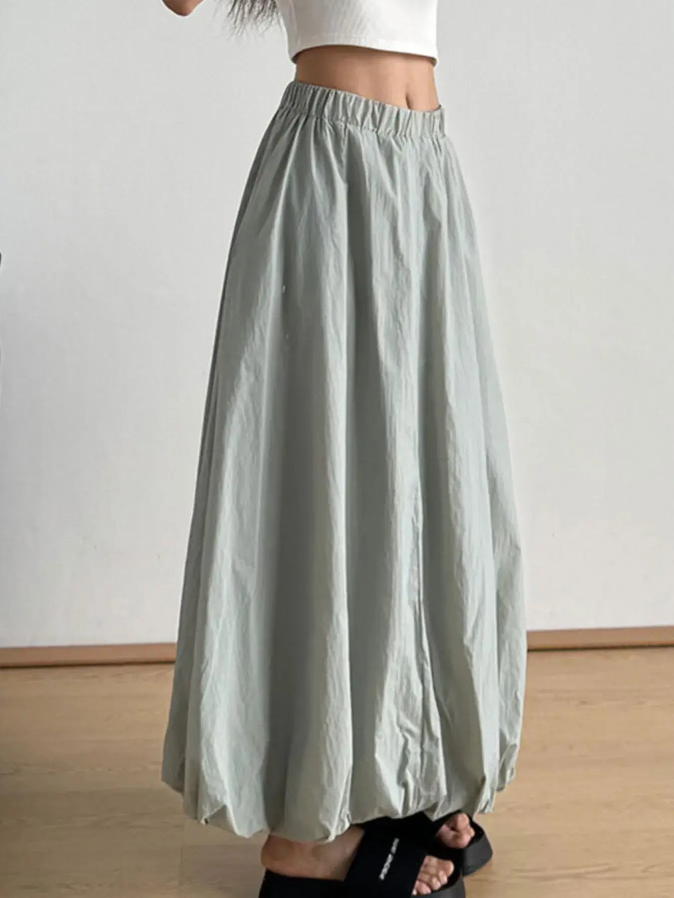 Woman wearing an elastic waist bubble hem maxi skirt in light grey with a flattering paperbag waist and modern silhouette.