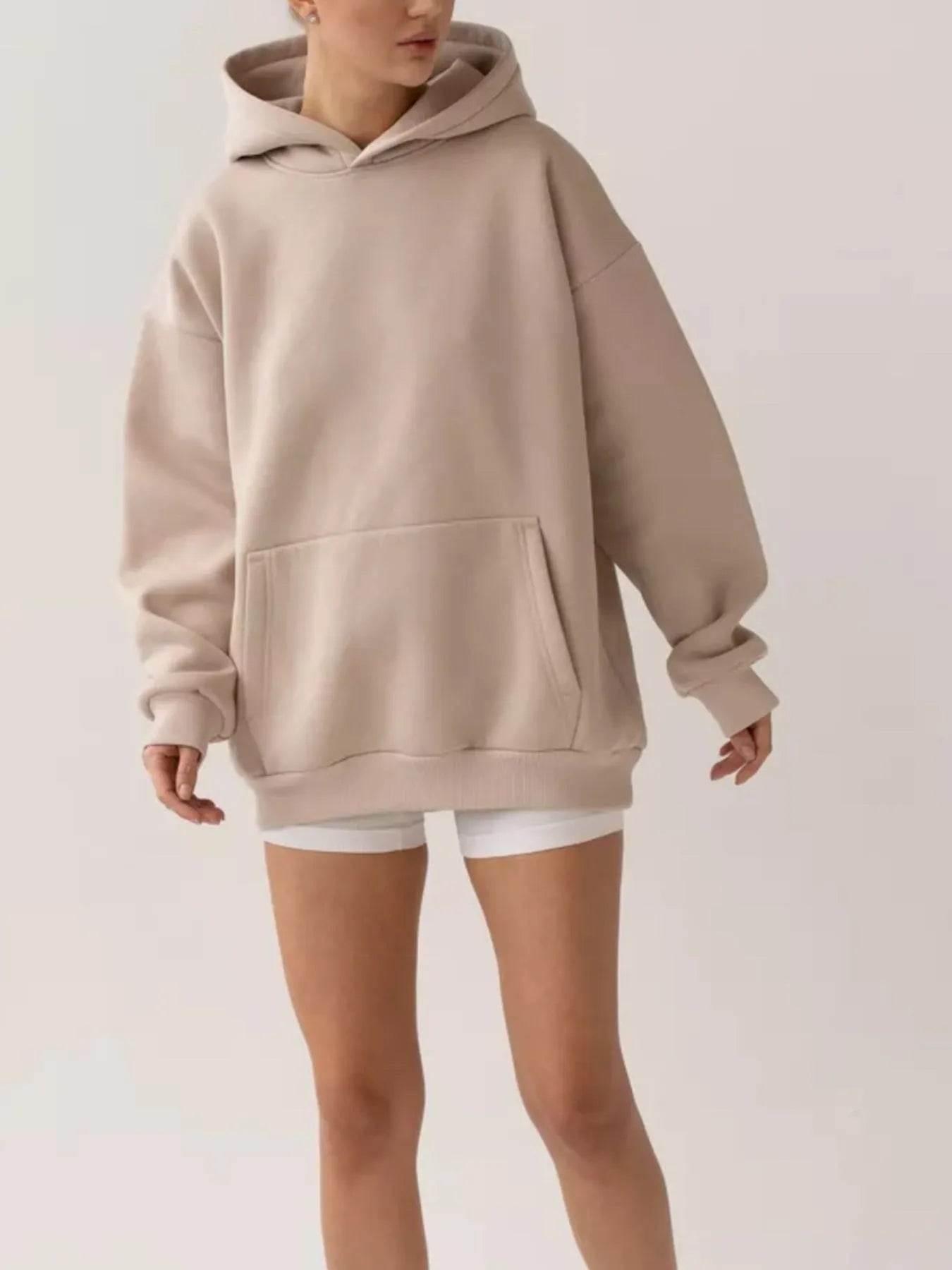 Woman wearing beige long sleeve kangaroo pocket hoodie, showcasing comfort and style with soft fabric and relaxed fit.
