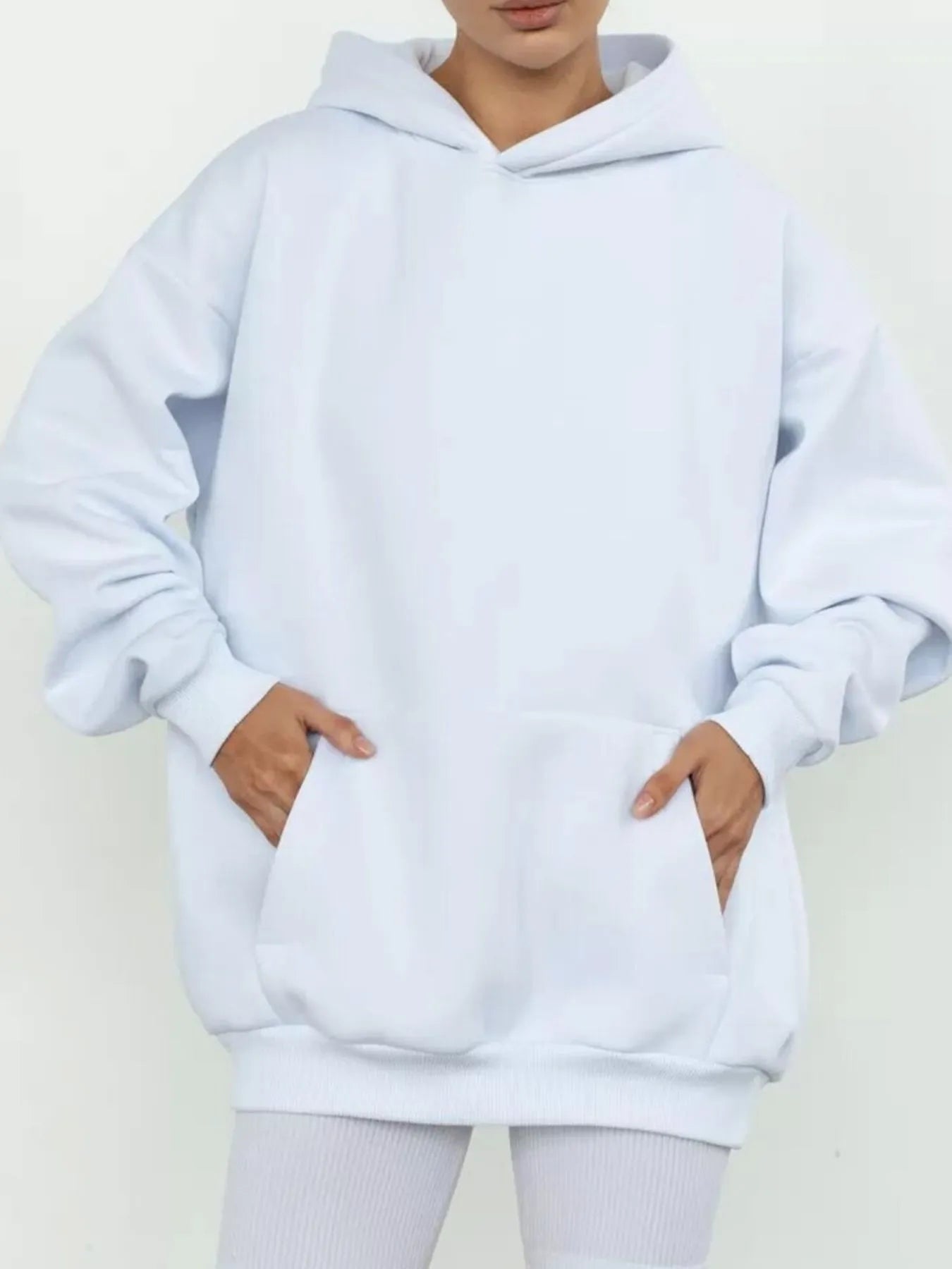 Woman wearing kangaroo pocket long sleeve hoodie in soft white, showcasing comfort and style with convenient pocket design.