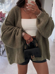 Woman wearing oversized olive green cardigan with dropped shoulders and voluminous sleeves, styled with white crop top and black bag.