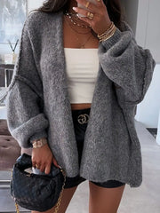 Woman wearing oversized grey open front dropped shoulder cardigan with textured design, styled with white crop top and black accessories.